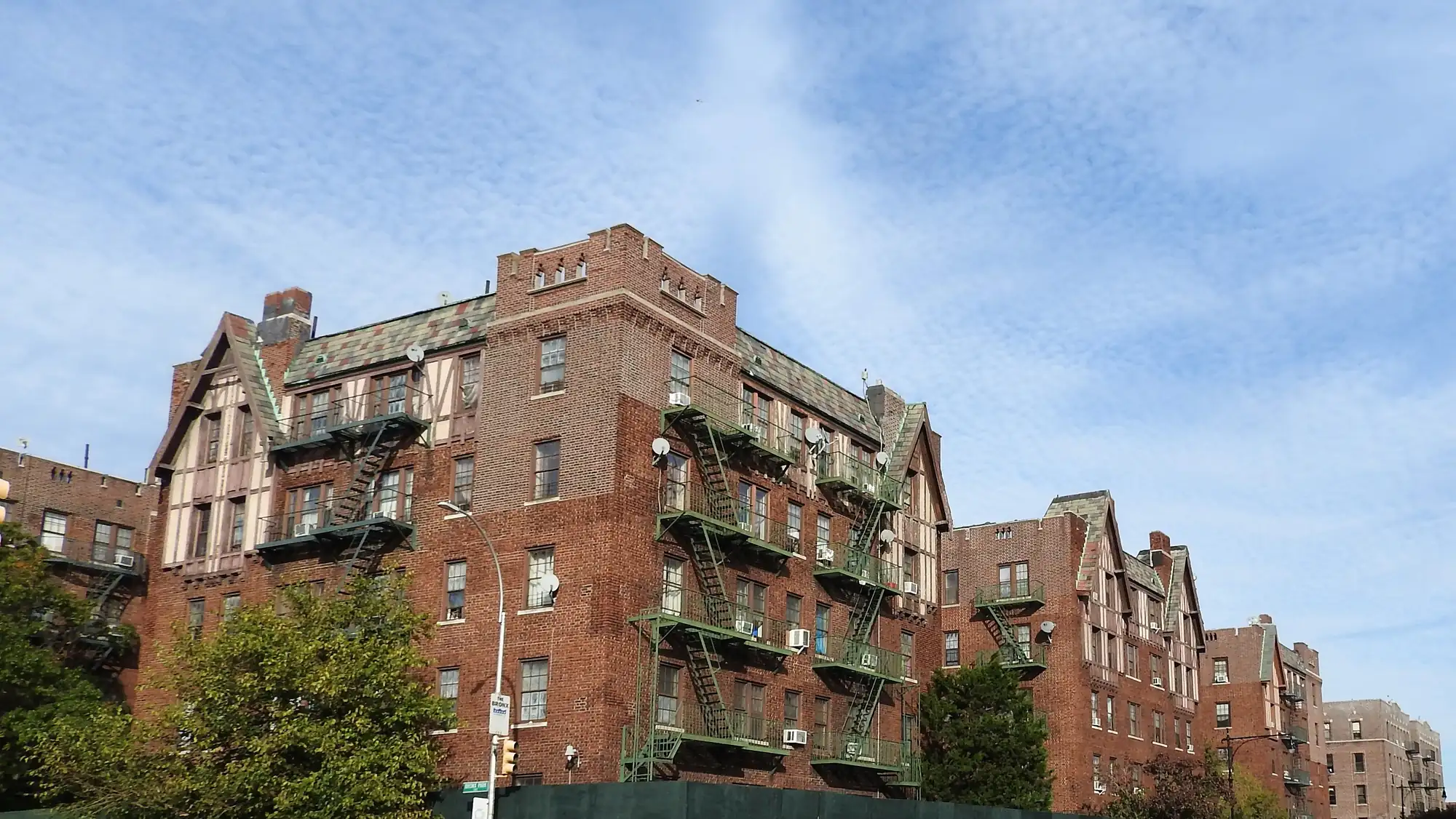 Brick apartment buildings with fire escapes at Bronx Park East and Allerton Avenue under a blue sky