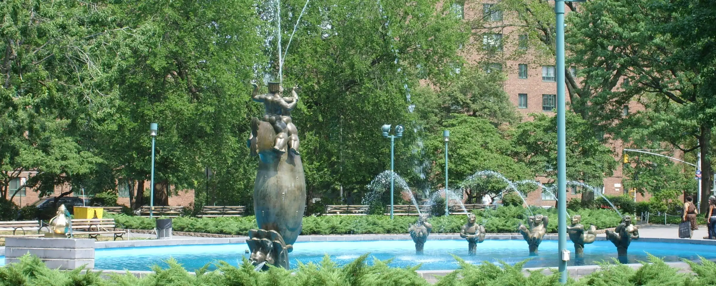 The fountain at the Parkchester oval with red and white flower beds on a sunny summer day