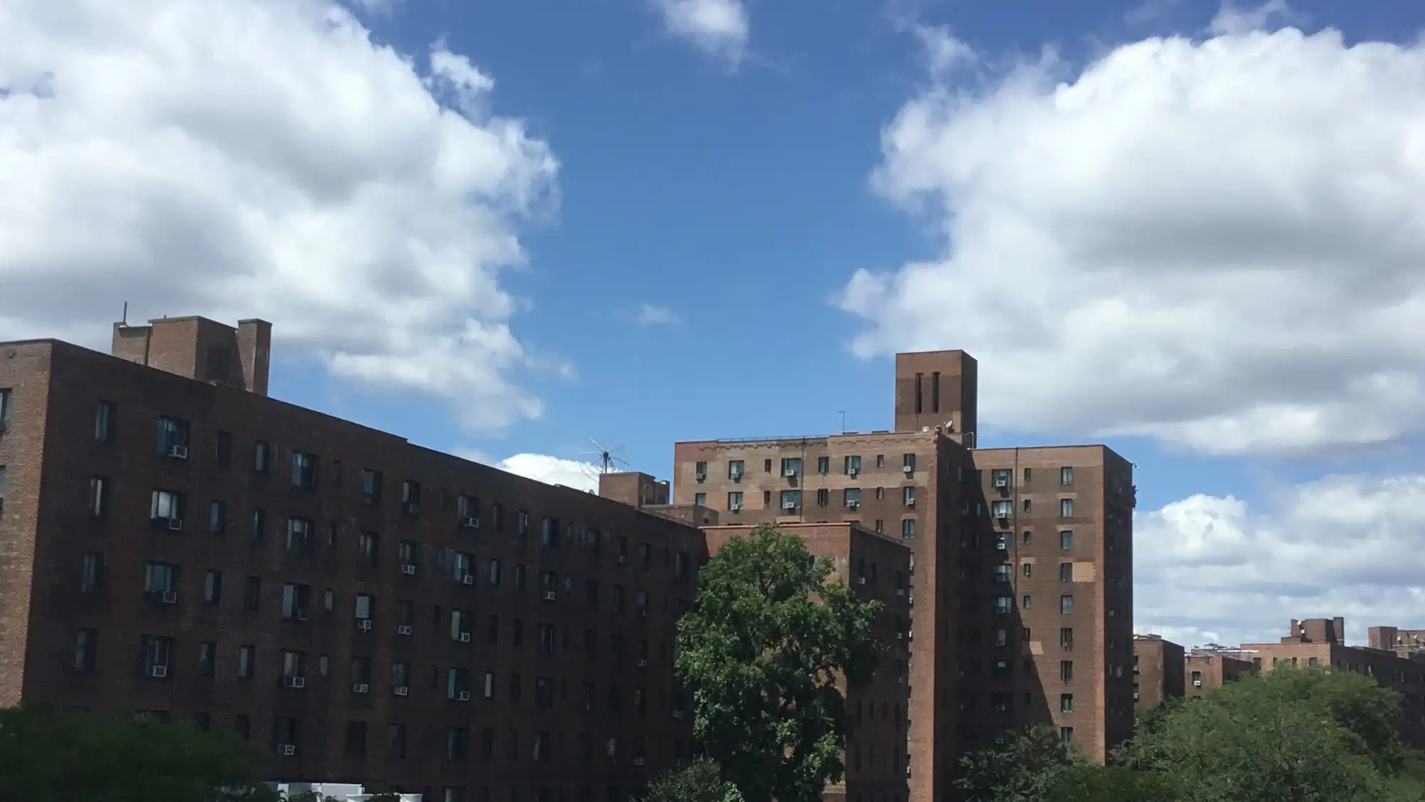 Brick apartment buildings of Parkchester under a blue sky with white clouds, seen from the 6 train