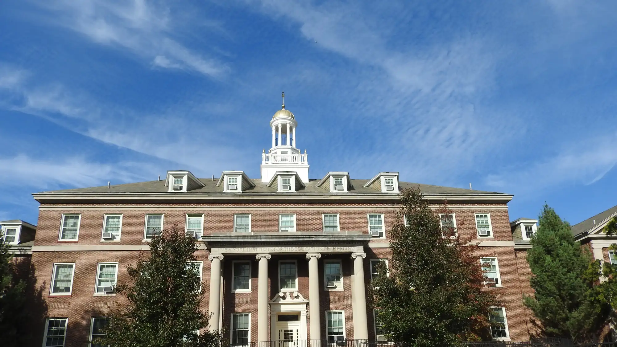 The New York Institute for Special Education building at 999 Pelham Parkway North, under a blue autumn sky