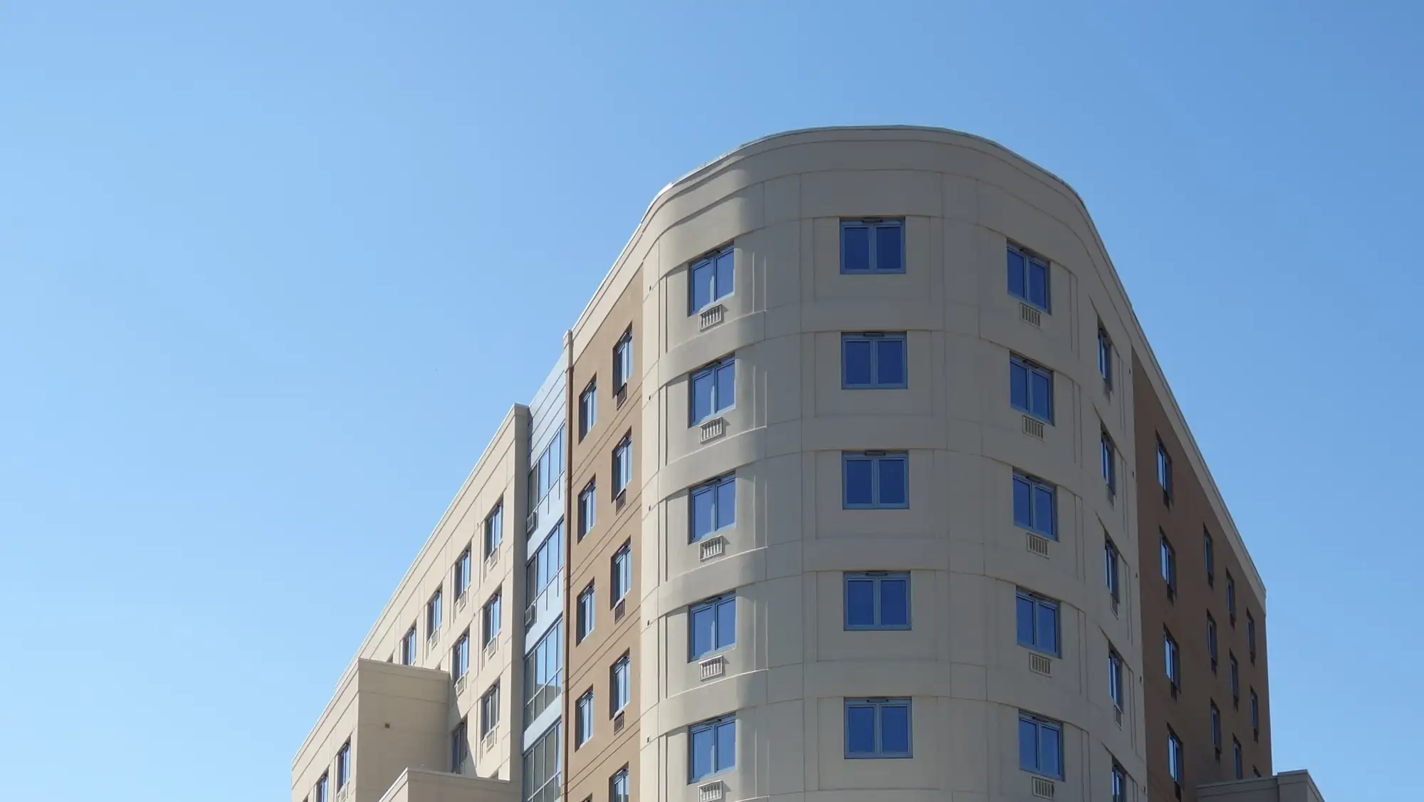 The curved upper floors of the apartment building at 1939 West Farms Road against a blue sky
