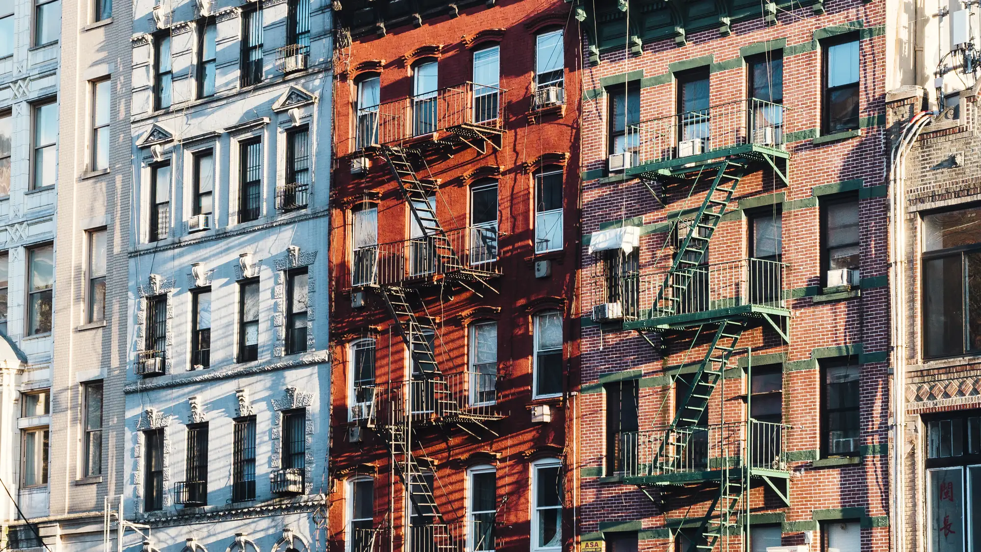 Row of classic New York brick apartment buildings with fire escapes in warm afternoon light